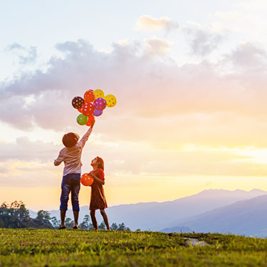 Ansicht zweier Kinder mit Luftballons mit Berglandschaft im Hintergrund  